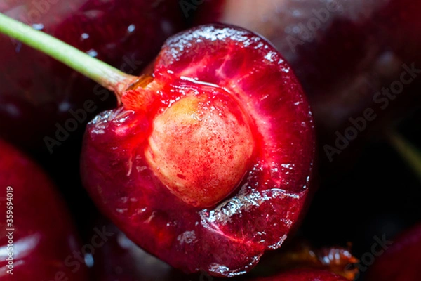 Fototapeta Closeup ripe red cherry, juicy berry cut into half with stone, on background of other fruits. Horizontal macro shot for wallpaper, postcard or creative design.