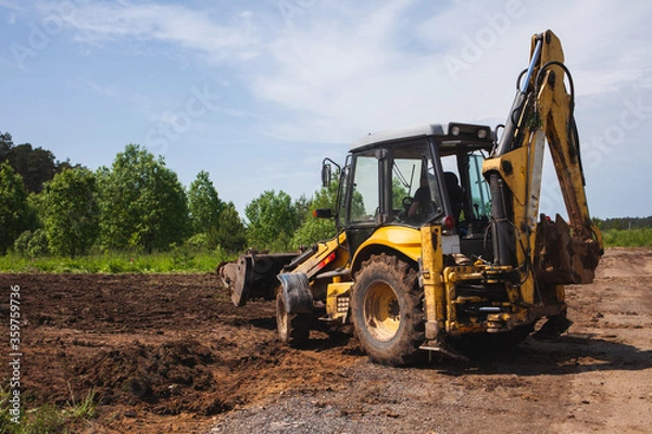 Fototapeta Clearing and leveling a private land plot. Yellow excavator driven earth in a wide bucket, back view