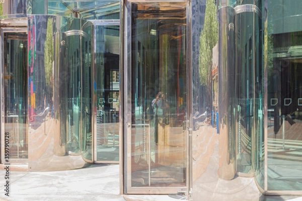 Obraz A yellow sculpture, trees, concrete, chrome, blue sky and the photographer provide colorful reflections in revolving doors of the JP Morgan Chase Tower in downtown Houston