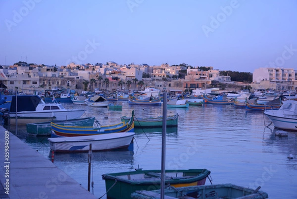 Fototapeta Multi-colored fishing boats rest in the sea bay against the background of a small old golden city and a blue cloudless sky.