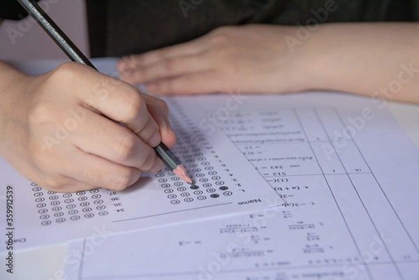 Fototapeta Students hand holding pencil writing selected choice on answer sheets and Mathematics question sheets. students testing doing examination. school exam.