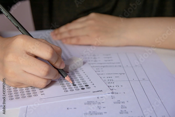 Fototapeta Students hand holding pencil writing selected choice on answer sheets and Mathematics question sheets. students testing doing examination. school exam.