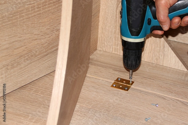 Fototapeta master twists the screw with an electric screwdriver into copper connecting loops, furniture connections, furniture assembly concept, handmade, hobby, homework