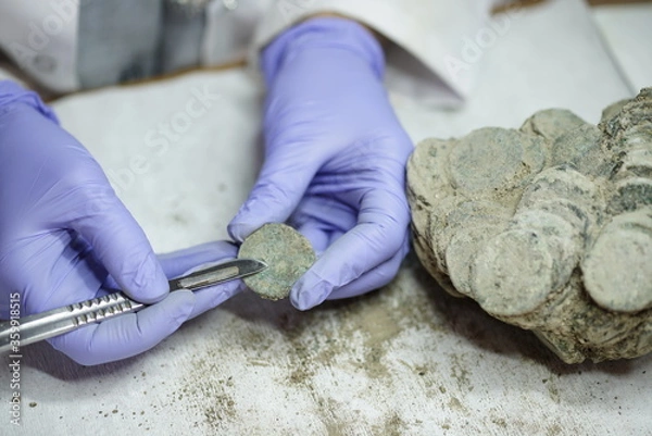 Obraz woman restoring ancient coins . Restorer, conservation. Archaeological background.