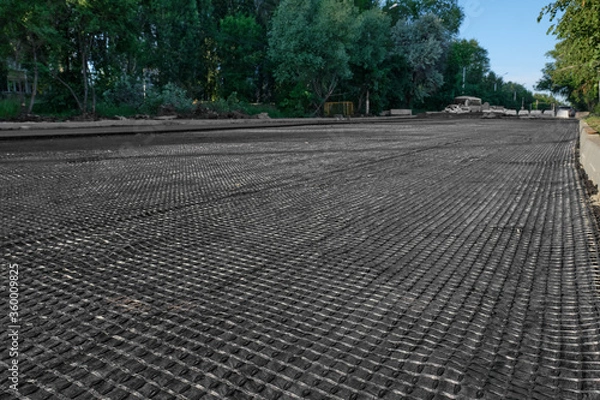 Fototapeta The construction of the road, laying of geomesh on soil before the asphalt pavement. Geogrid reinforcing a new roadbed, modern technologies.