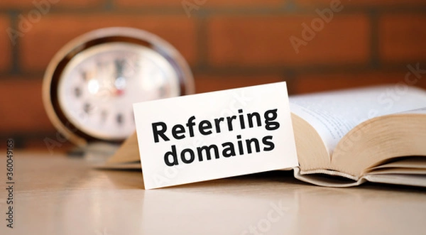 Fototapeta Referring domains - concept text on a white background with a clock and an open book