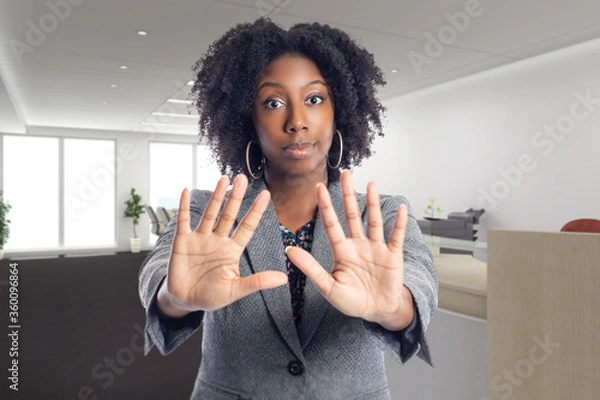 Fototapeta Businesswoman holding hands up as a stop gesture to tell co-workers to stay away and keep social distancing in the office or workplace because she is scared