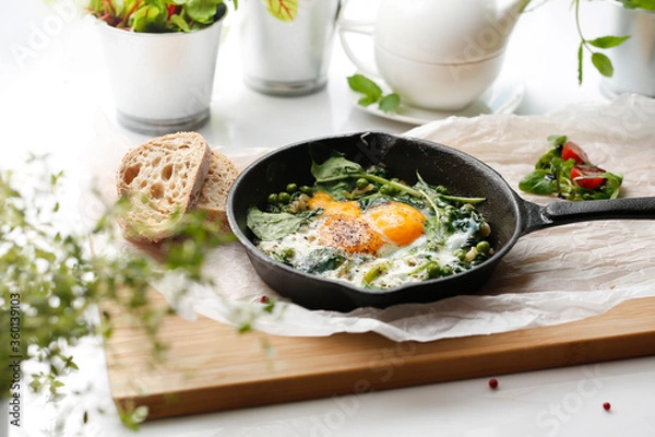 Obraz Eggs with green peas and spinach baked in a pan. Ready dish served in a hot pan. Suggestion of serving the dish. food background