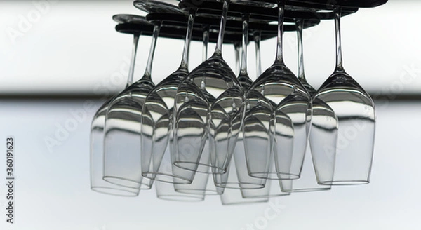Fototapeta Many empty crystal wine glasses hanging upside down on a special rack over the counter of a bar.