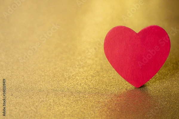 Fototapeta One single red heart  on a gold glitter and sequin background that sparkles and has lots of copy space for love and Valentine's Day