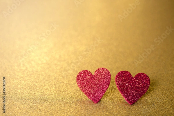 Fototapeta Two red hearts like a couple on a gold glitter and sequin background that sparkles and has lots of copy space