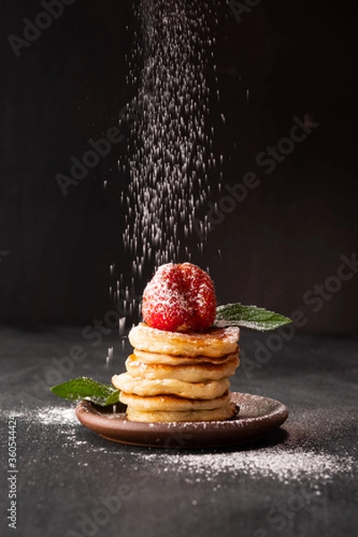 Fototapeta powdered sugar sprinkles on tiny flakes of pancakes with strawberries, mint and honey on a black background. Fashionable food. Mini cereal pancakes. Pancake porridge.