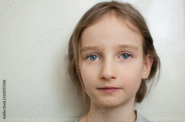 Fototapeta Portrait of a little girl with long blond hair and blue eyes with ponytail is standing on white background in studio