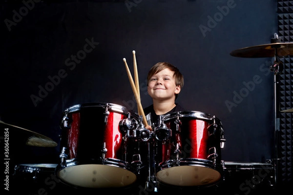 Fototapeta The child sits with drumsticks in his hands. Studying in the studio.