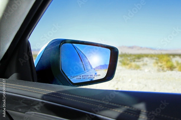 Fototapeta Car rear-view mirror with sun reflection with warning "Objects in mirror are closer than they appear" - view on the landscape in Death valley National Park from car window