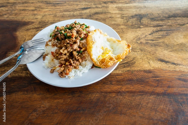 Obraz Rice topped with stir-fried pork and basil in  white dish on wooden table. , Text space.