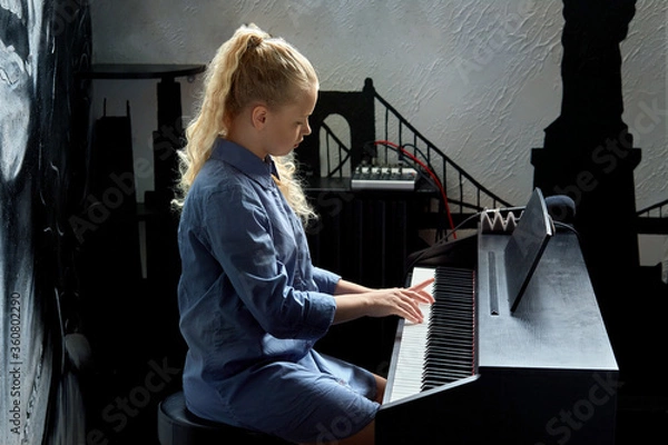 Fototapeta Side view of a young blonde girl playing the piano in the studio.