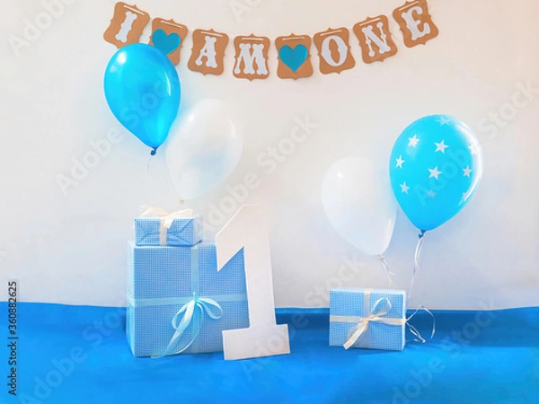 Obraz One year birthday decorations set. Decoration for a boy holiday party. Bunch of blue & white balloons, gift boxes, large white kappa board number one shape, and sign with the inscription I am one"."