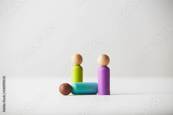 Fototapeta Wooden figures concept. Brown colour skin person lying on the ground with two white people standing around. Untold age or gender. Racial concept