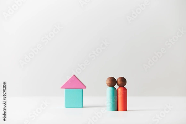 Fototapeta Wooden figurines concept. Two wooden figures people standing in front of a tiny block house, black skin colour, young couple. Realty market. Centred