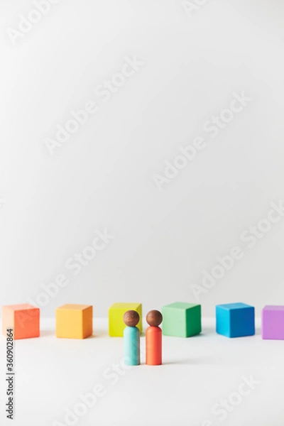 Fototapeta Wooden figures concept. Couple standing in front of wooden blocks in colours of the gay pride rainbow flag. Couple of dark skin colour. 