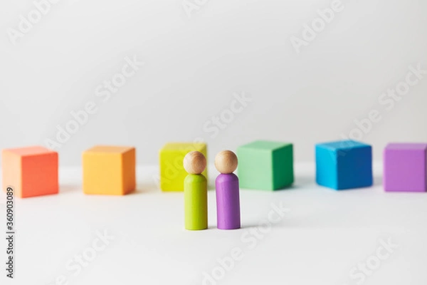 Fototapeta Wooden figures concept. Couple standing in front of wooden blocks in colours of the gay pride rainbow flag. Couple of white skin colour. 
