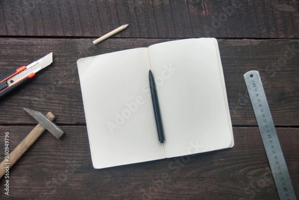 Fototapeta Building tools and opened notebook on dark wooden board. Copy space, flat lay
