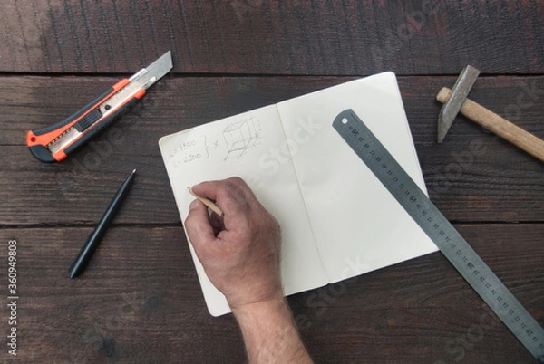 Fototapeta Building, architecture, construction concept. Flat lay of a male hand writting calculations in a notebook with building tools around