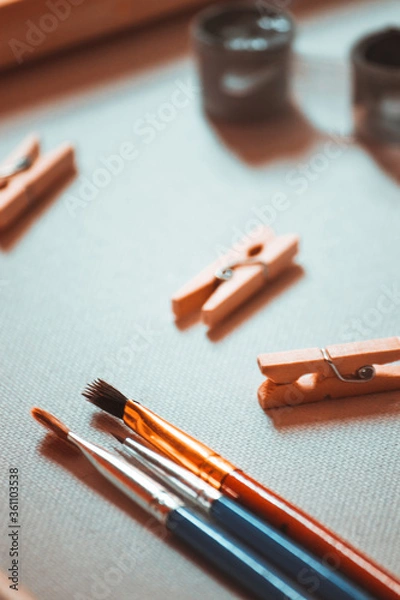 Obraz Three brushes of different shapes lie on a white canvas near paints and clothespins.