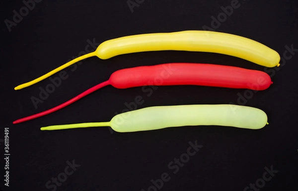 Fototapeta Three balls of yellow, lemon and red are on a black surface. The balls are long with the remaining unsneed ends
