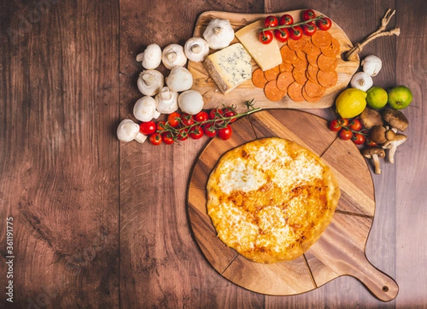 Fototapeta Homemade freshly baked Pizza Margherita with melted mozzarella on the top on a wooden board with lots of decorative vegetables. Concept of fresh hot pizza with free space for your text/decorations.