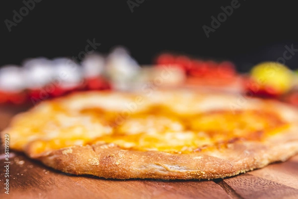 Fototapeta Homemade freshly baked Pizza Margherita with melted mozzarella on the top on a wooden board with lots of decorative vegetables. Concept of fresh hot pizza with free space for your text/decorations.