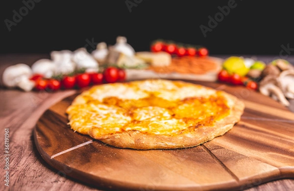 Fototapeta Homemade freshly baked Pizza Margherita with melted mozzarella on the top on a wooden board with lots of decorative vegetables. Concept of fresh hot pizza with free space for your text/decorations.