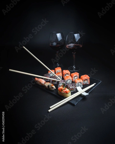 Fototapeta Sushi with red wine on a dark restaurant background. Chopsticks. A glass of wine. Soy sauce. Rolls and sushi. Japanese cuisine.