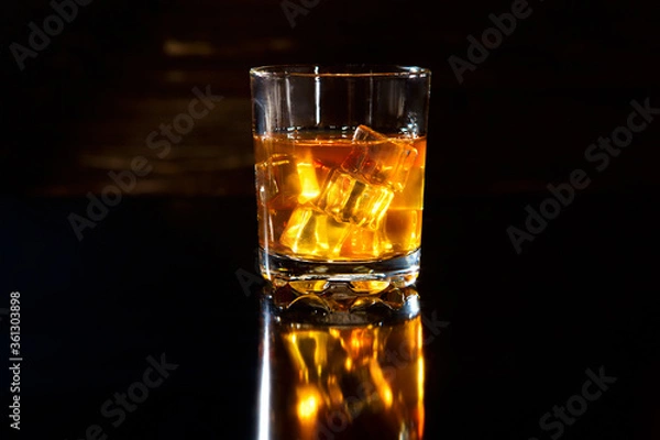 Fototapeta Glass of whiskey with ice cubes on black table