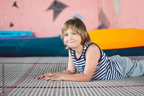 Obraz gymnast sitting on trampoline in fitness center. Tired child sits on trampoline after jumping while playing outdoors. Boy sit on trampoline in sport complex. Resting time and preparing for jumping