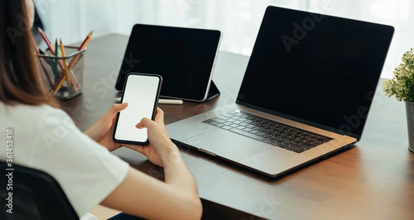Fototapeta Woman using digital laptop and tablet with smartphone on the table in house. Blank screen for advertising.