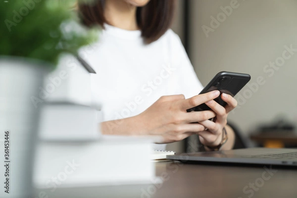 Fototapeta Young woman hand holding smartphone and chatting with friends at social network on the table.