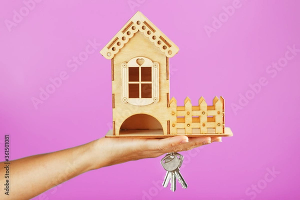 Fototapeta A small wooden house with keys in hand on a pink background.
