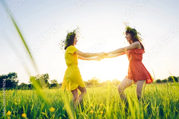 Obraz Two young girls in bright dresses are circling in the field. Summer evening in nature