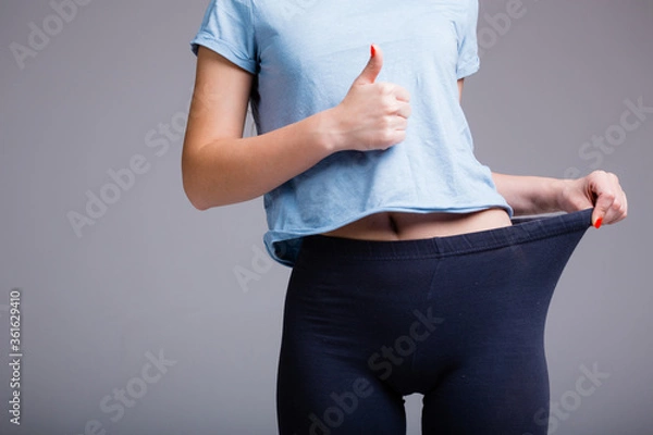 Obraz Closeup of the body of a girl who pulls leggings to the side and shows like as a sign that she has lost weight before vacation on a white background