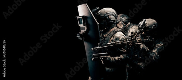 Obraz Portrait of a group of fighters of a special unit. They hide behind a bulletproof shield. Black background. Three soldiers. The concept of the fight against terrorism.