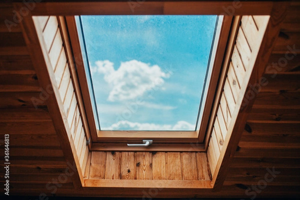 Obraz Blue bright sky with clouds through the roof window - natural light inside the house