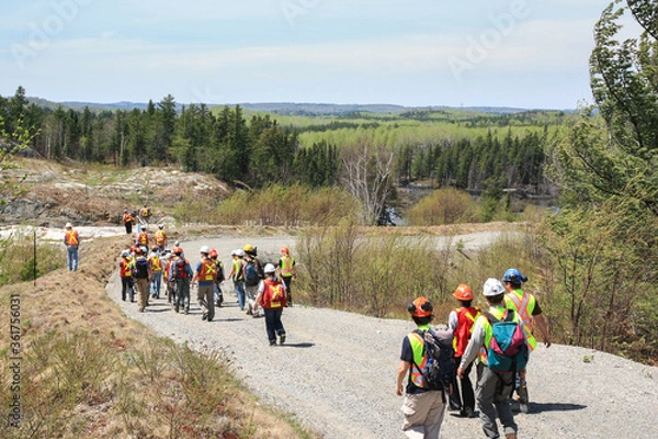 Fototapeta SUDBURY, ONTARIO, CANADA - MAY 21 2009: Group of workers and geologists in hardhats and high-visibility vests walking on road to geological outcrop site.