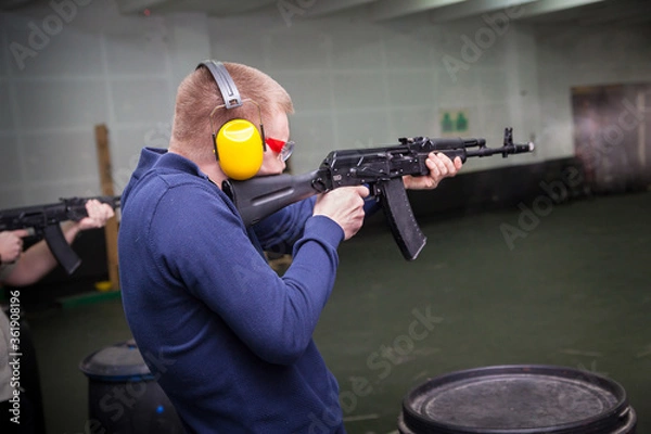 Obraz A man shoots a gun at a target in a dash with headphones