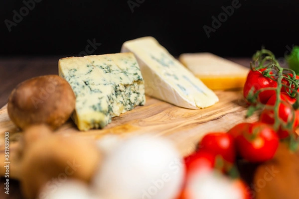 Fototapeta Blue cheese, goats cheese, and parmesan cheese on a wooden board along with tomato, basil, mushrooms. Concept of pizza ingredients with free space for your decoration/text.