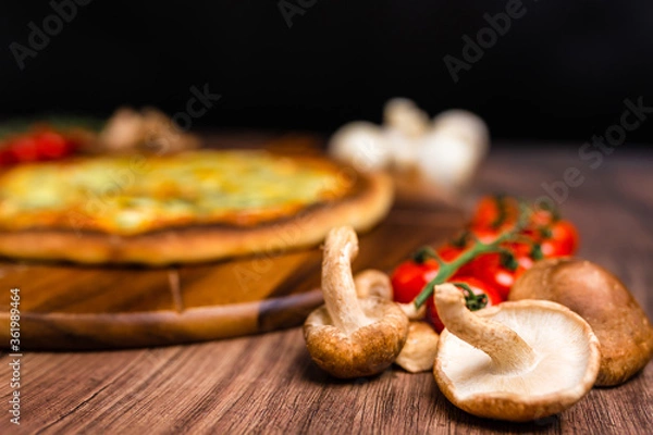 Fototapeta Close-up british mushrooms on a wooden table with pizza in background. Mushroom ingredient for pizza. Concept of preparing pizza with British mushrooms.