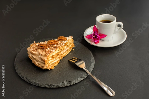 Obraz A typical Portuguese cake made of cookies "Maria" called Bolo de Bolasa with cream, pecans, black and white chocolate, on a black slate with a fork, with espresso and a flower on a black background
