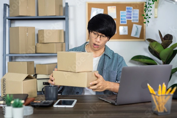 Obraz Asian business man startup SME entrepreneur working in a cardboard box prepares delivery box for customer