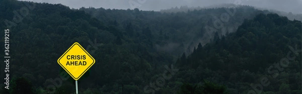 Obraz Crisis ahead sign is located in front of misty and foggy mountains